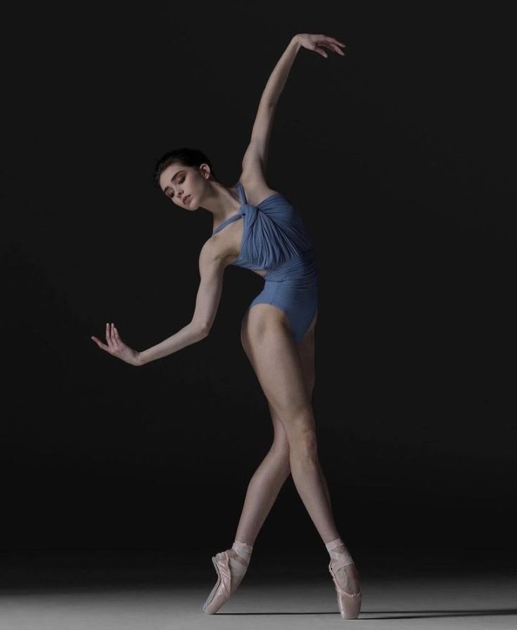 a woman in a blue leotard and ballet shoes is standing on one leg