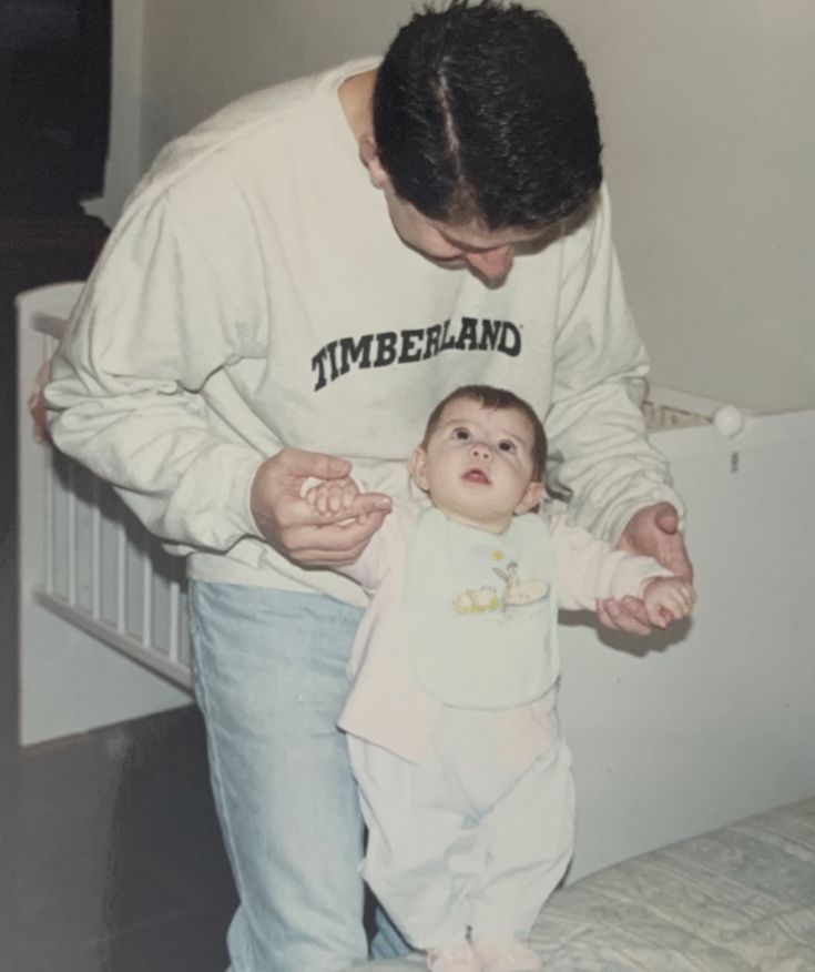 a man holding a baby in his arms while standing next to him on top of a bed