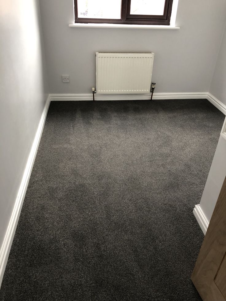 an empty room with a radiator, window and carpeted floor in it