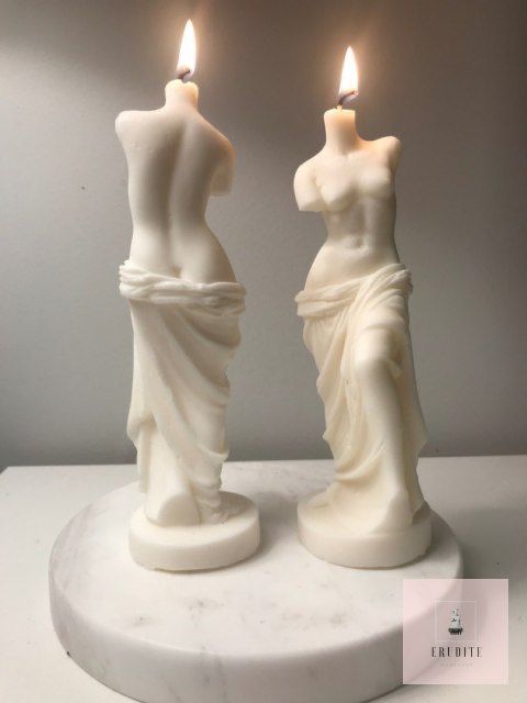 two candles that are sitting next to each other on a white surface with the candle lit in front of them