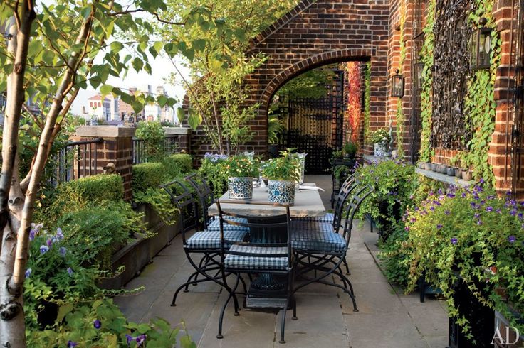 an outdoor dining area with potted plants on the patio and brick archway in the background