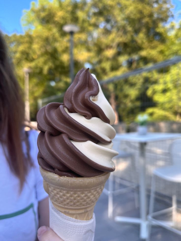 a close up of a person holding an ice cream cone with chocolate and white icing