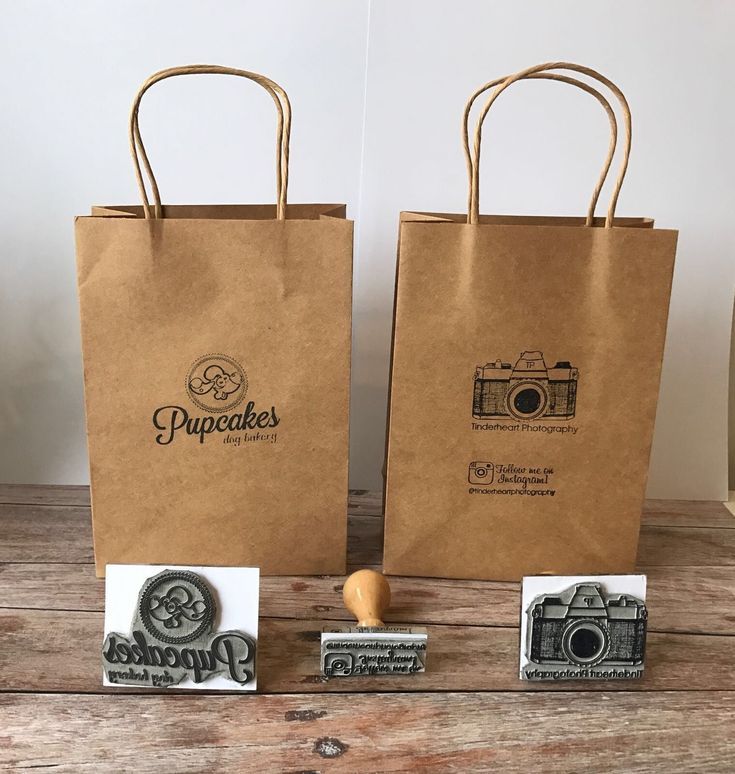 two brown paper bags sitting next to each other on top of a wooden table with rubber stamps