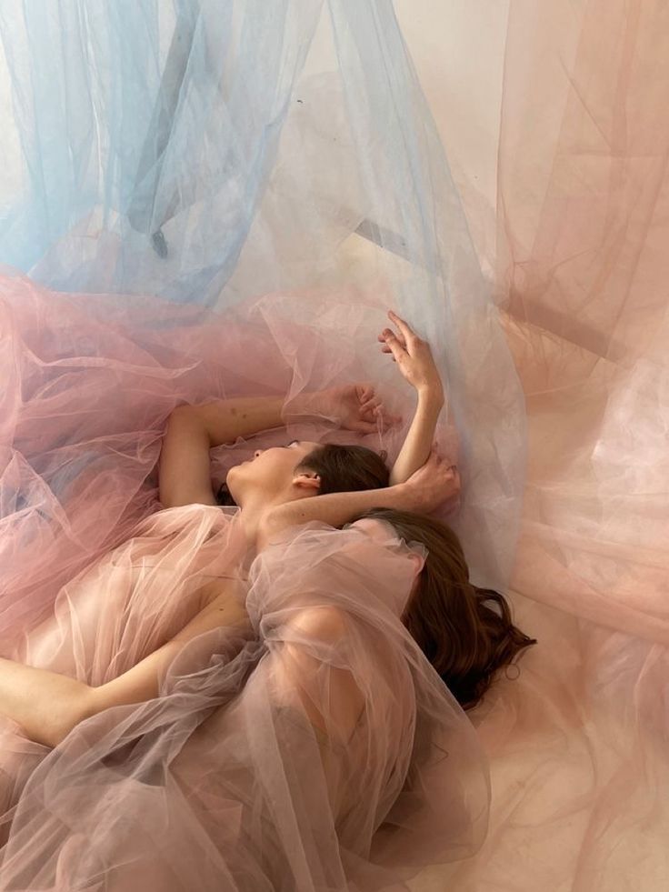 a woman laying on the ground in a pink dress with sheer fabric covering her body