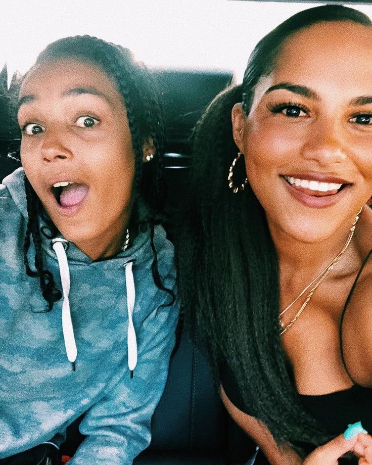 two women sitting in the back seat of a car, one with her tongue out