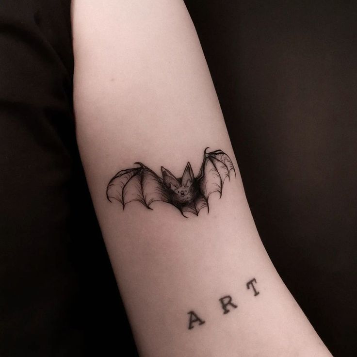 a small bat tattoo on the arm that says arr in cursive font