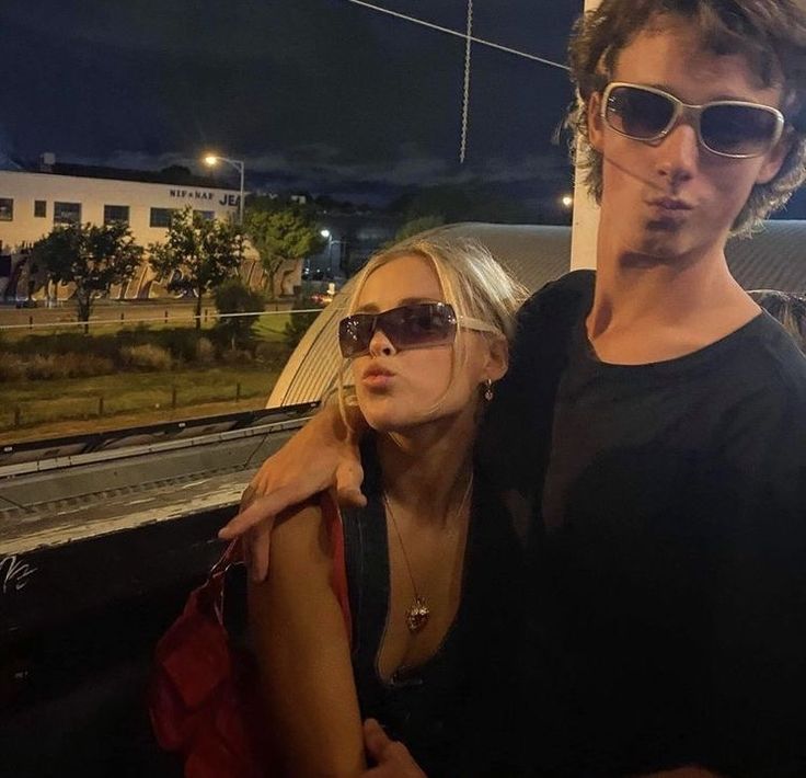 a man and woman standing next to each other on a train platform at night time