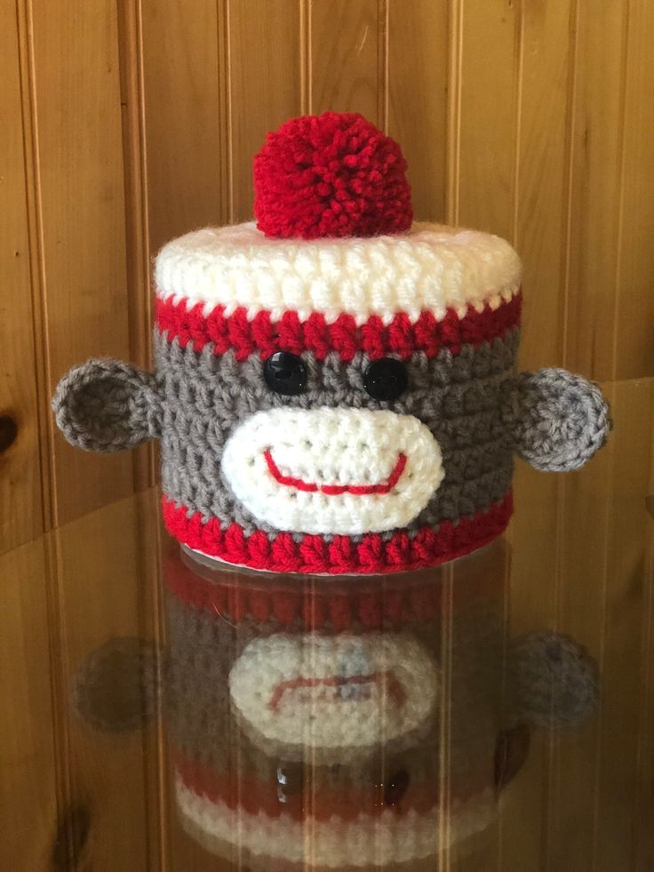 a crocheted sock monkey with a red hat on it's head sitting in front of a wooden wall