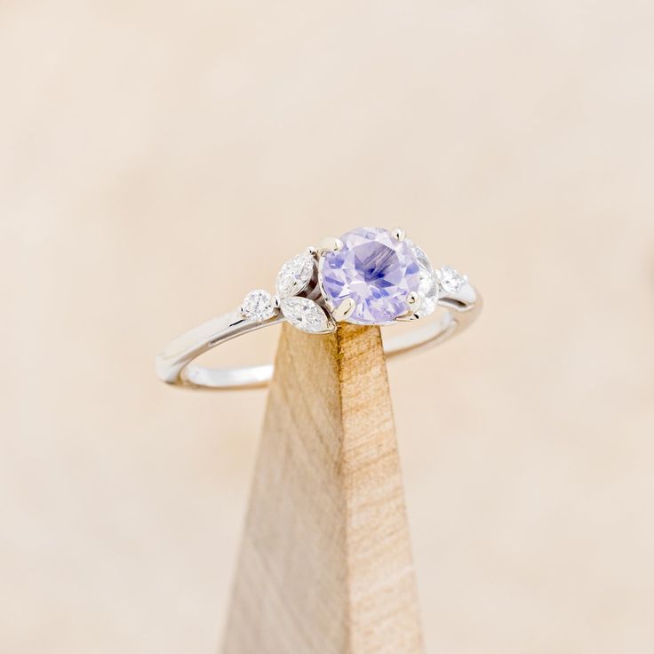 a tan and white diamond ring sitting on top of a wooden stand