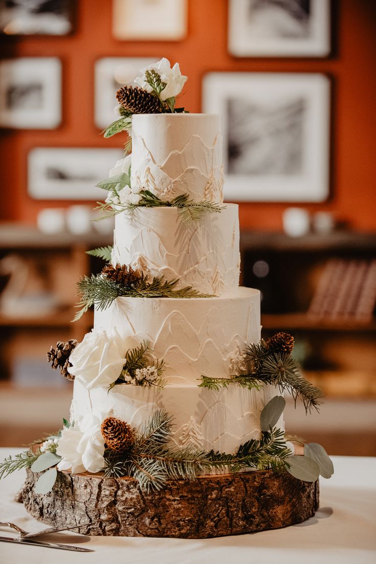 a white wedding cake with pine cones and greenery