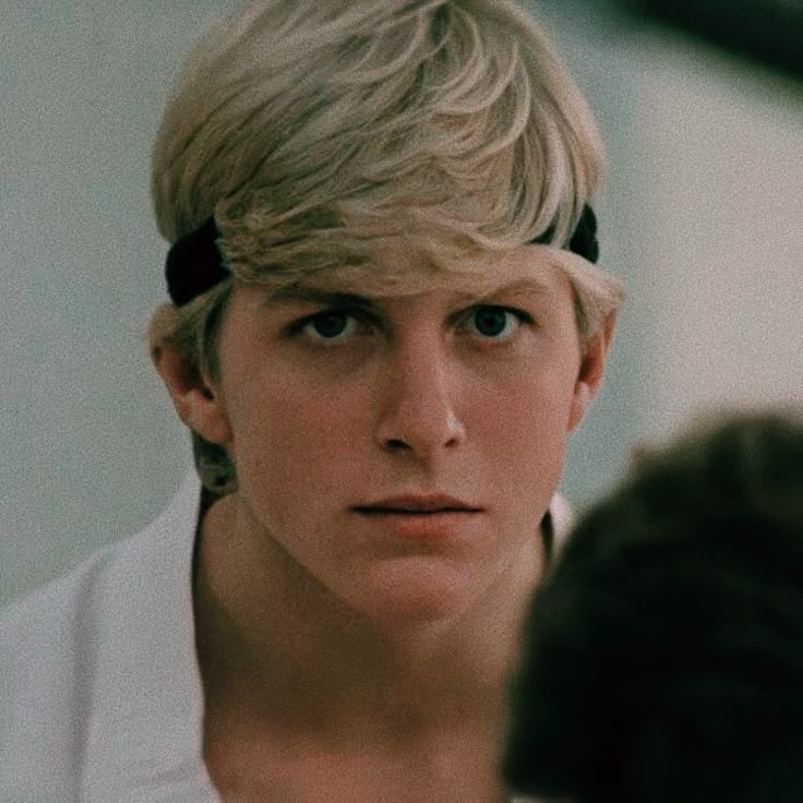 a young man with blonde hair wearing a white shirt and black bow tie looking at his reflection in the mirror