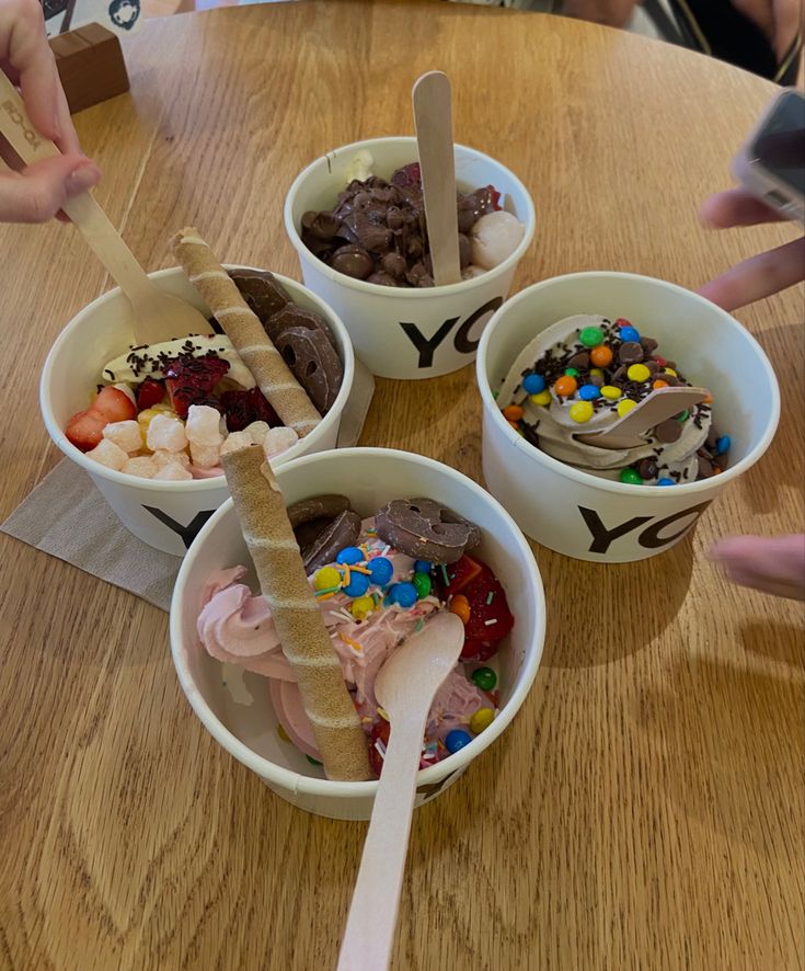 three ice cream bowls filled with different types of toppings on top of a wooden table