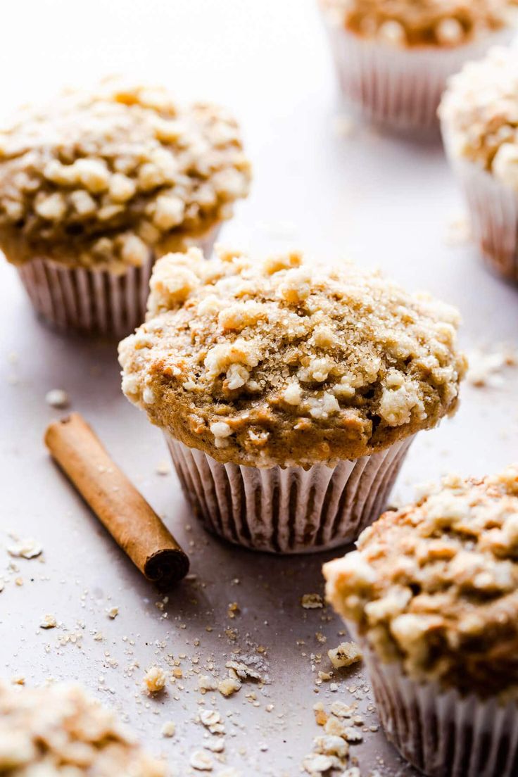 several muffins with cinnamon on top are sitting on a white surface next to an orange and brown stick