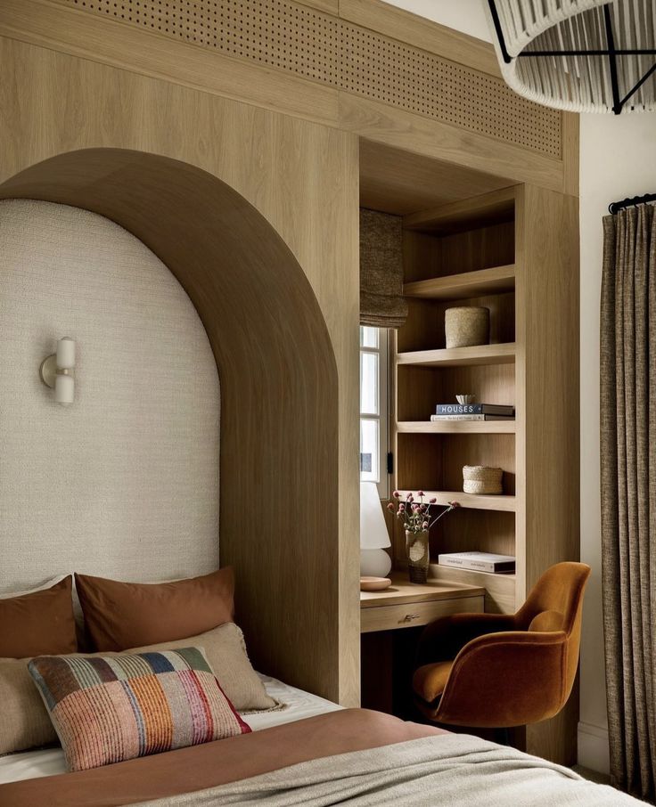 a bed sitting under a window next to a wooden desk and book shelf in a bedroom