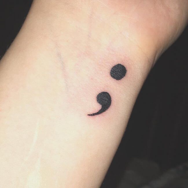 a small wrist tattoo with two black dots on the middle of it and a smiley face