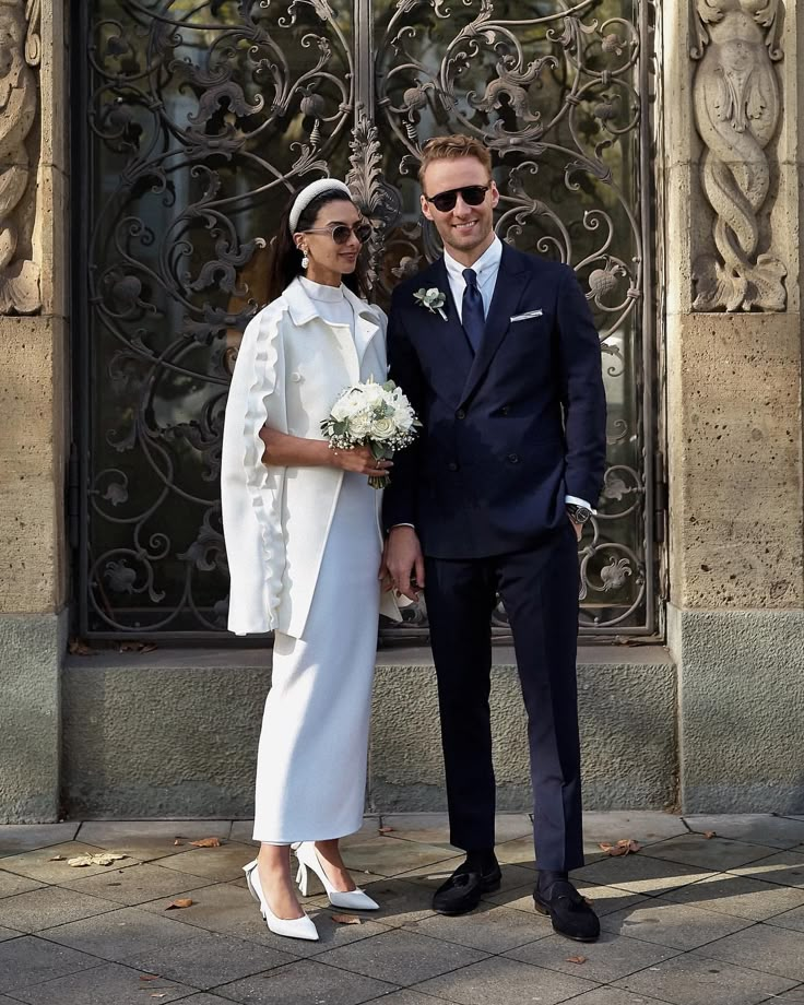 a man and woman standing next to each other in front of a building with ornate iron doors