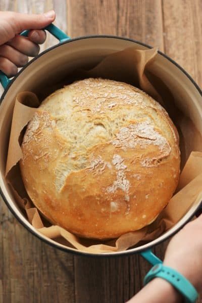 a loaf of bread sitting in a pan on top of a wooden table next to a person's hand