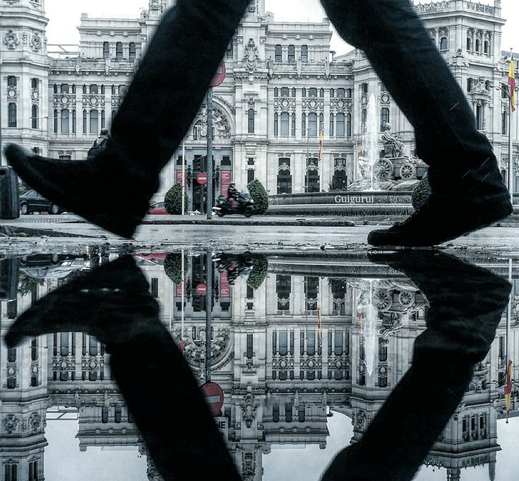 a person standing in front of a building with their feet up on the ground and reflecting in the water