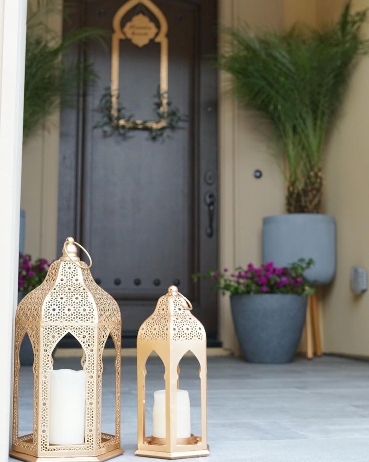 two white candles are sitting on the front porch with potted plants in the background