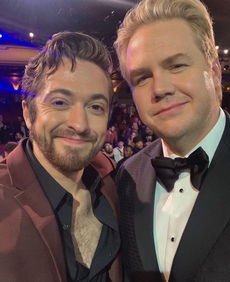 two men in tuxedos posing for a photo at an event with the audience