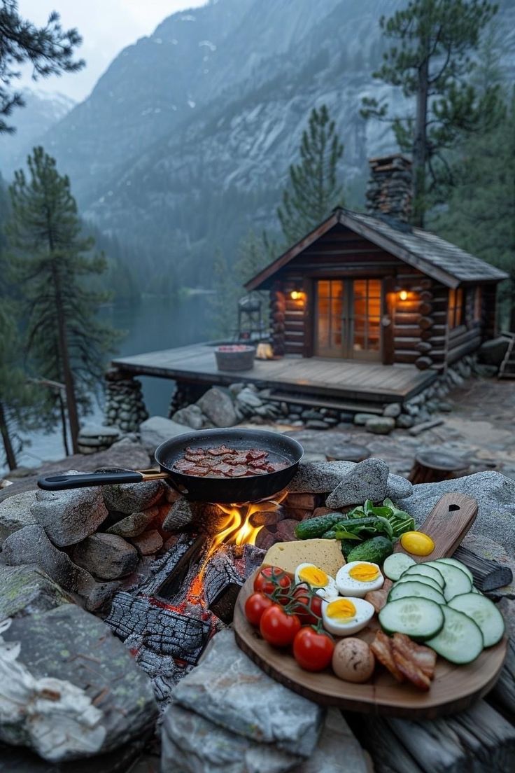 an outdoor grill with vegetables and meats on it in front of a log cabin