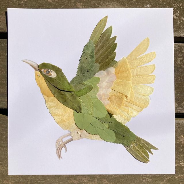 a bird made out of paper sitting on top of a piece of paper with leaves