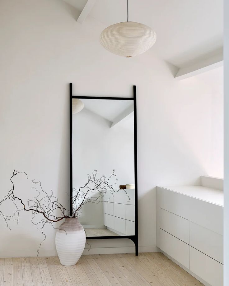 a white vase sitting on top of a hard wood floor next to a large mirror