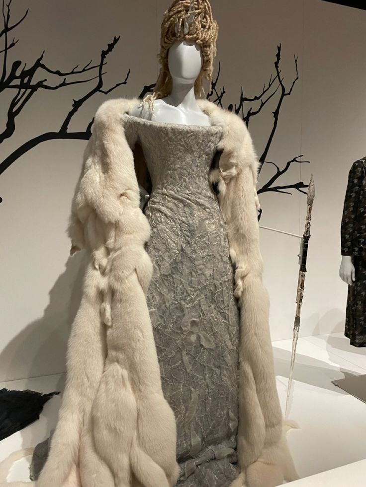 a dress and fur coat on display in a room with mannequin's