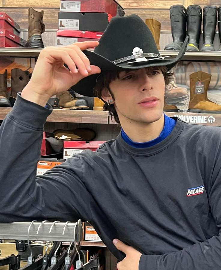 a young man wearing a black cowboy hat in a shoe store with his hands on his head