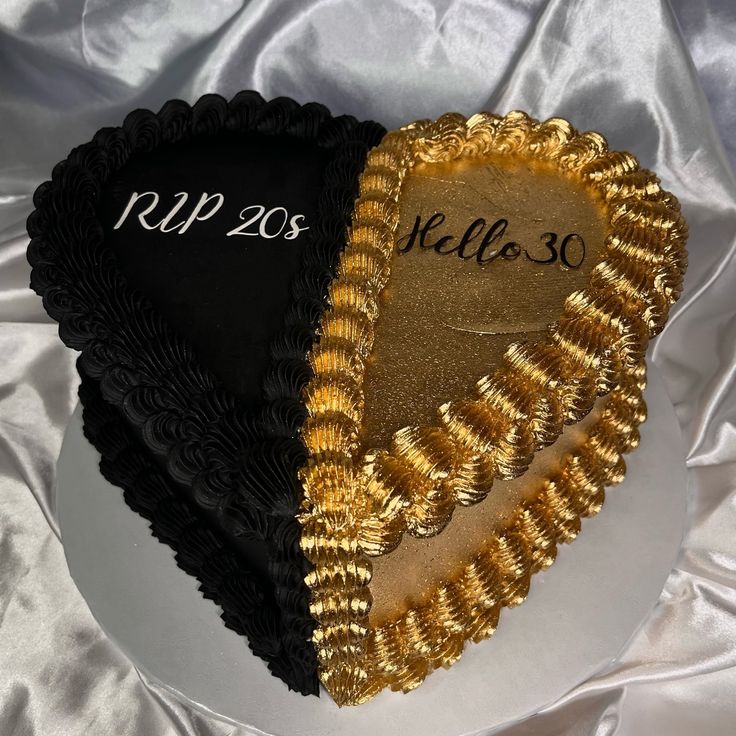 two heart shaped cakes sitting on top of a white table cloth covered in gold and black frosting