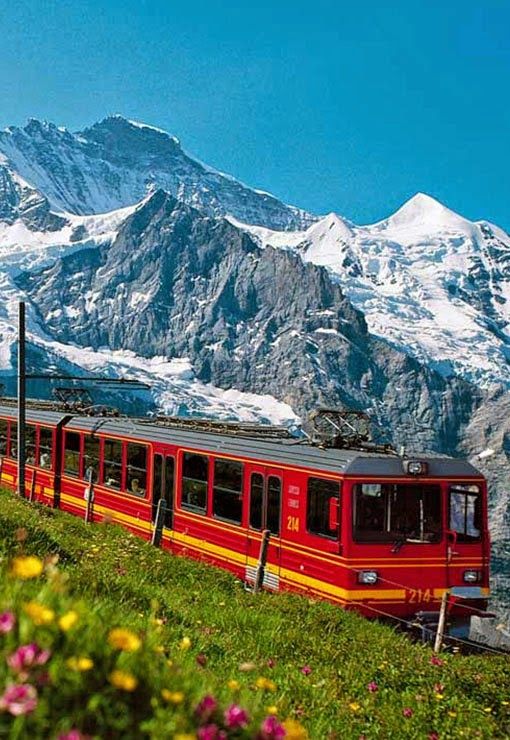 a red and yellow train traveling down tracks near snow covered mountain range in the distance