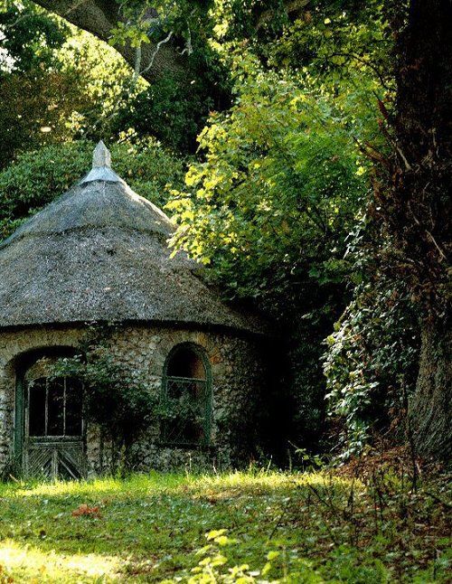 an old stone building with a thatched roof in the middle of trees and grass