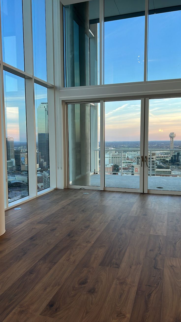 an empty room with wooden floors and large windows looking out onto the city skyline at sunset