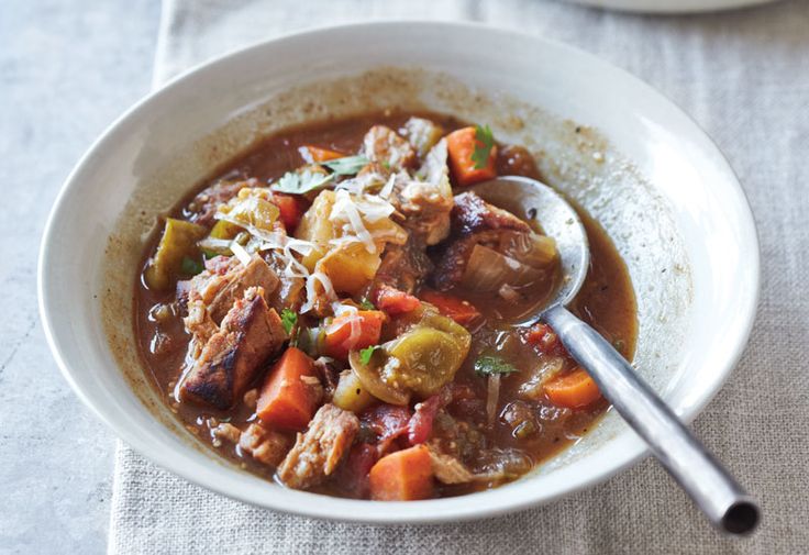 a white bowl filled with meat and vegetable soup on top of a cloth covered table