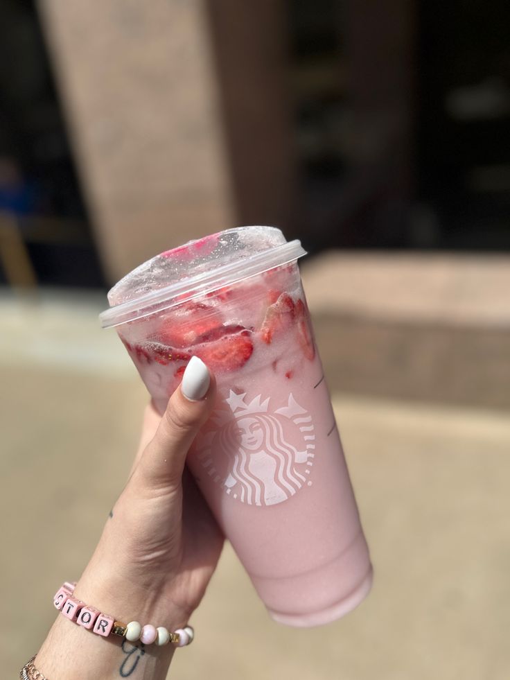 a woman holding up a pink starbucks cup with strawberries in it's sleeve