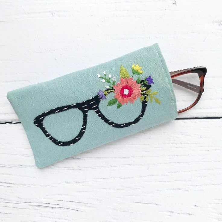 a pair of glasses sitting on top of a blue cloth covered case with flowers and leaves