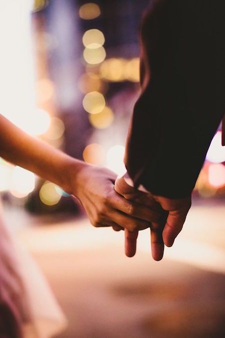 black and white photograph of two people holding each other's hands with blurry lights in the background