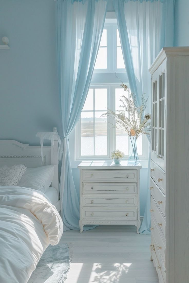 a white bed sitting next to a window in a bedroom under a blue shade curtain