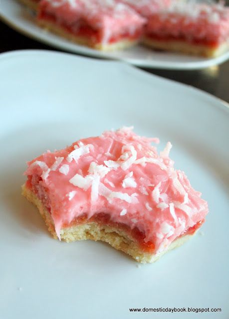 two white plates topped with pink frosting and coconut bars on top of each other