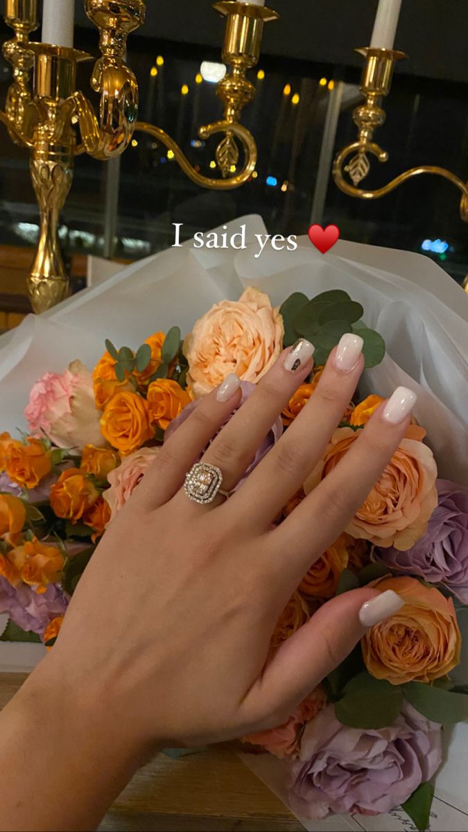 a woman's hand with pink and yellow flowers on her wedding day, next to a gold candelabra that says i said yes