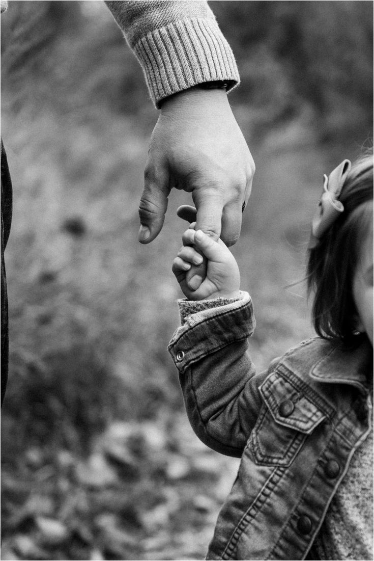 a black and white photo of a child holding the hand of an adult's hand