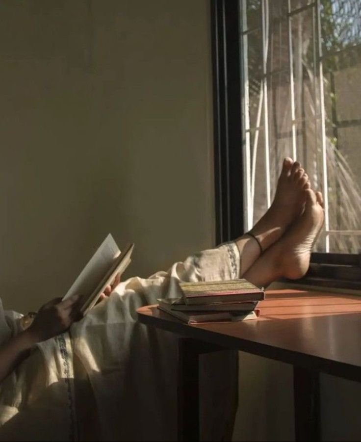 a person sitting at a desk with their feet up on a table and reading a book