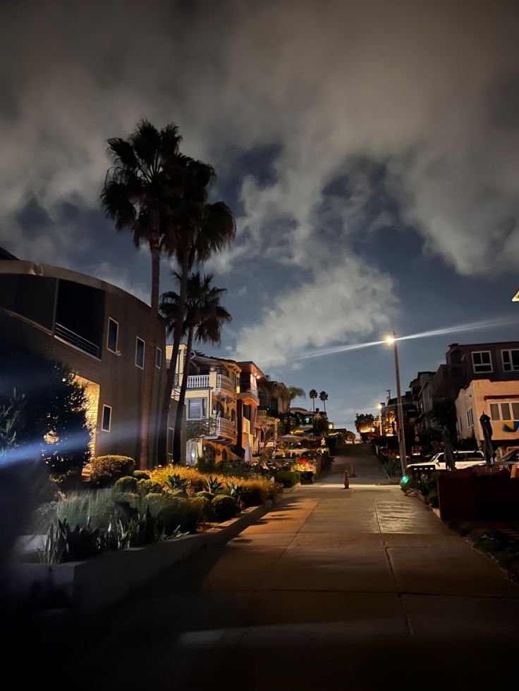 an empty street at night with palm trees in the foreground and clouds in the background