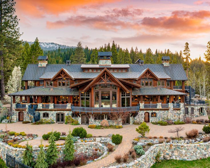 a large house surrounded by lots of trees and rocks in front of a sunset sky