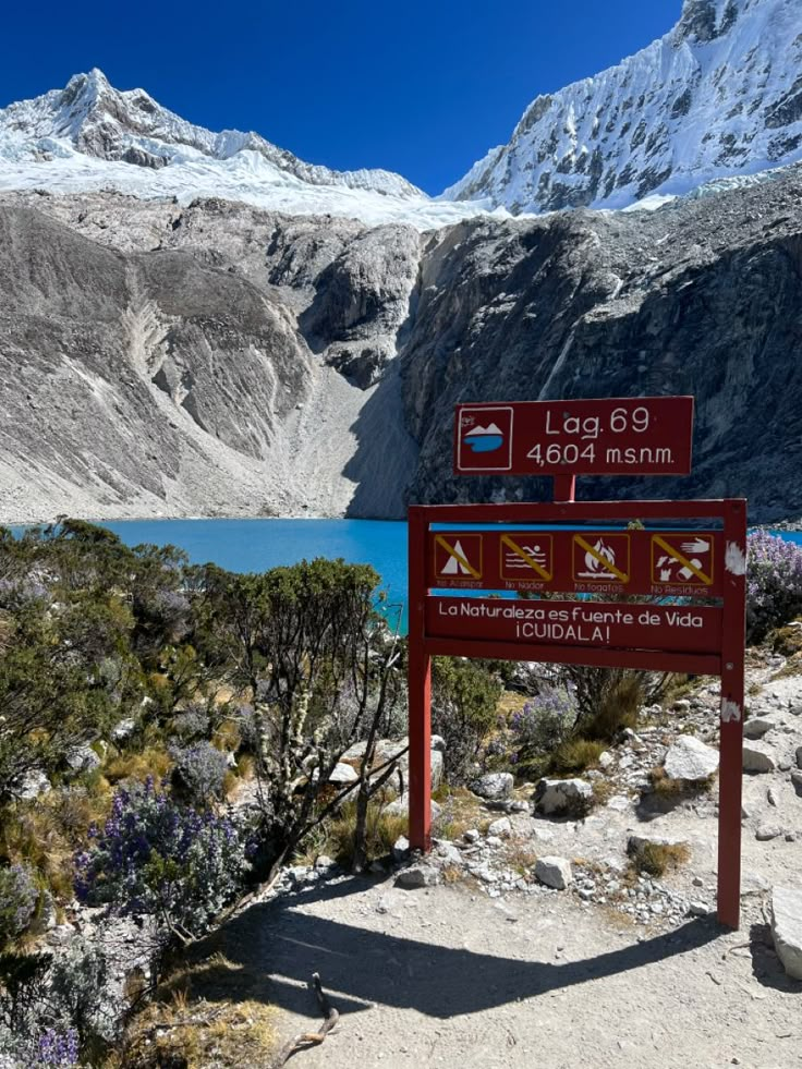 a red sign sitting on the side of a mountain next to a body of water