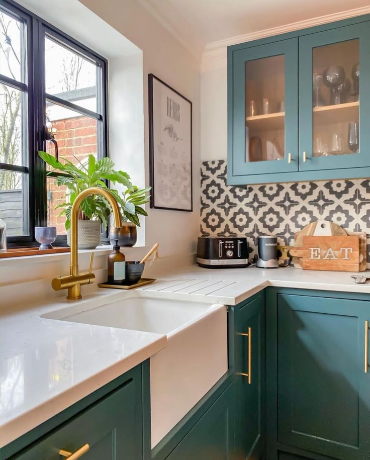 a kitchen with green cabinets and white counter tops, along with a gold faucet