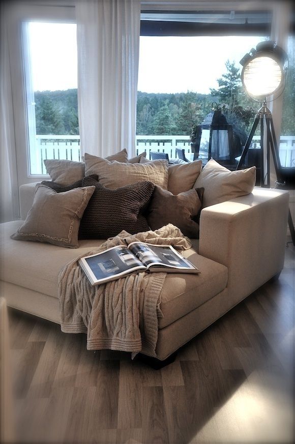 a couch with pillows and blankets on it in front of a window that is open