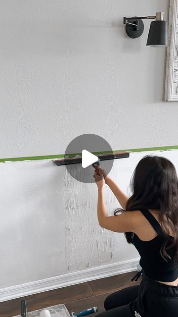 a woman sitting on the floor working on a wall