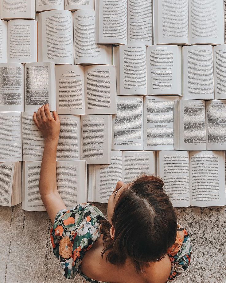 a woman laying on the ground next to an array of open book's in front of her