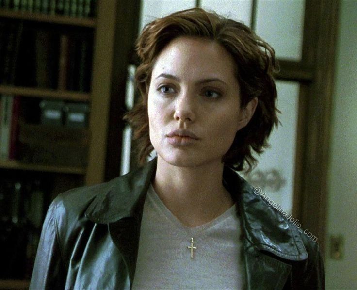 a woman wearing a cross necklace standing in front of a bookshelf